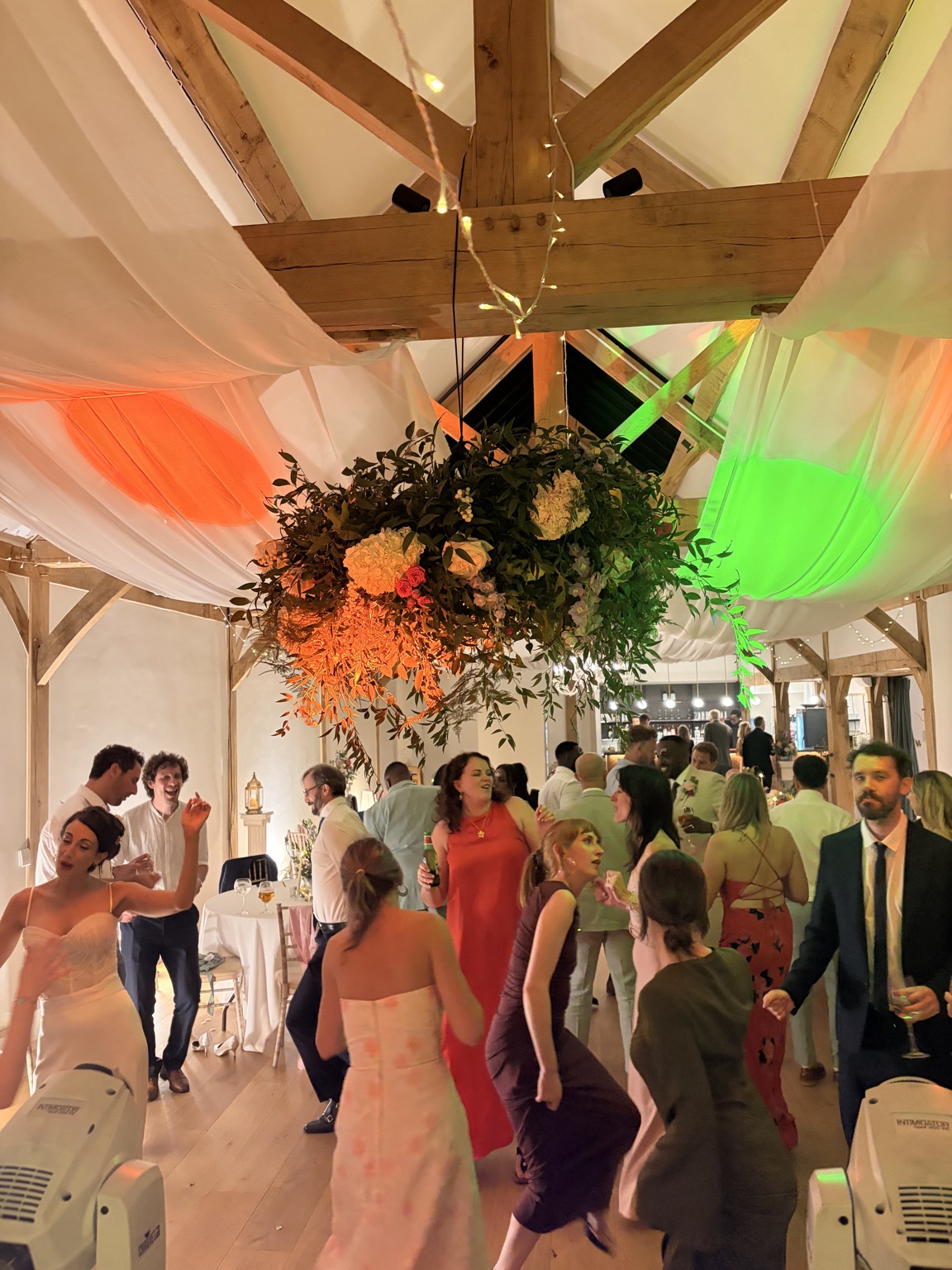 kat-hash-alfriston-gardens-dancing Wedding guests dancing beneath the hanging flowers and coloured lights at Alfriston Gardens
