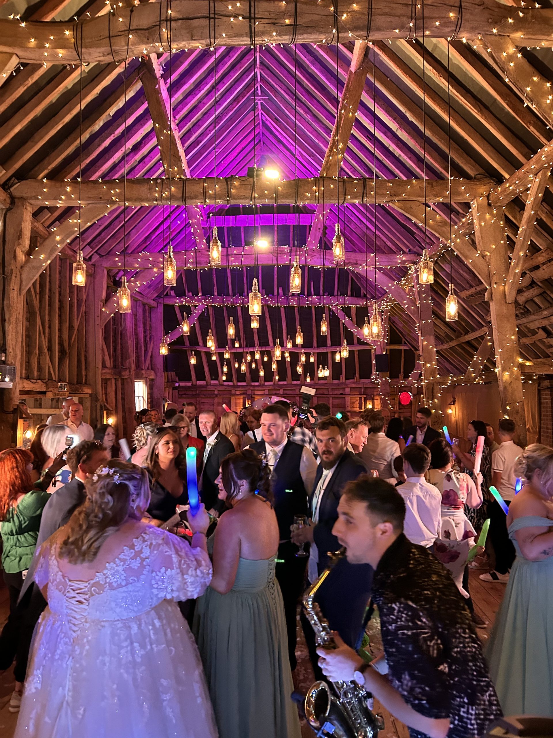sdc-crowd Wedding guests dancing beneath purple venue lighting in a timber barn